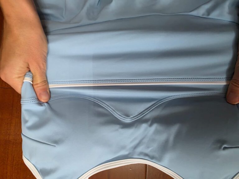 Hands holding a blue yoga garment to examine its fabric, seams and white trim